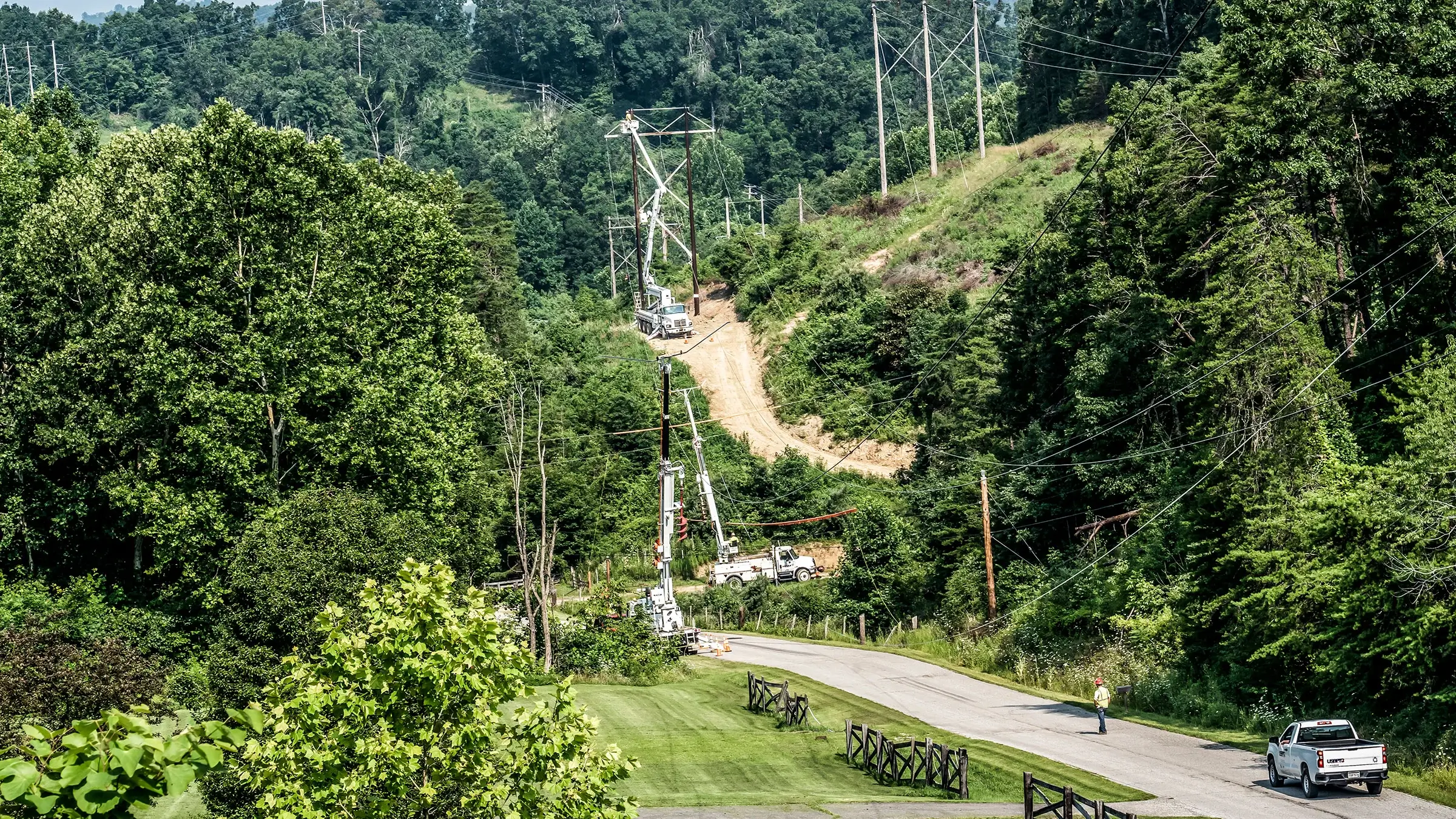 Power crew works on power lines following a road and path through forest like area