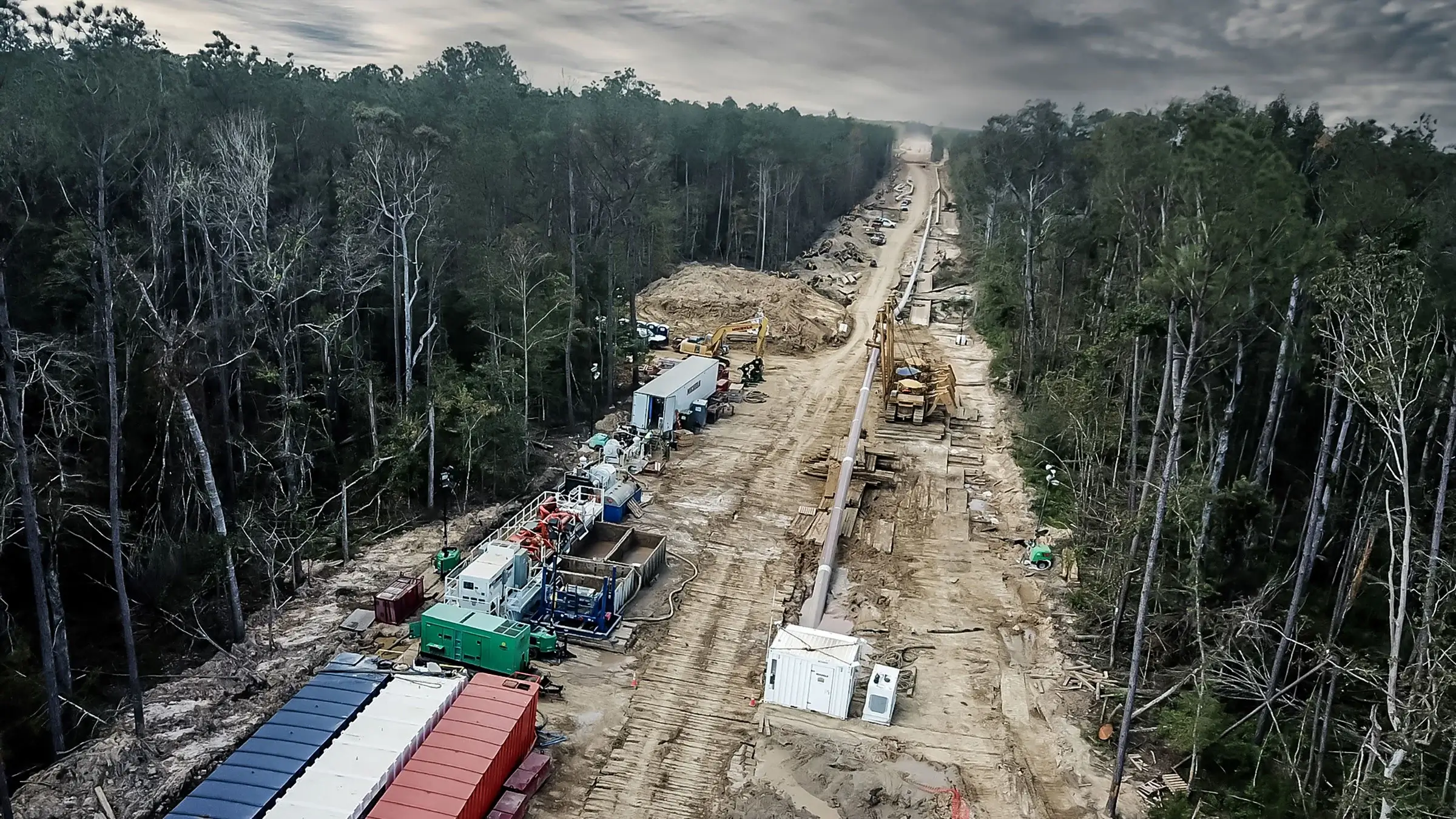 A large pipeline being driven into the ground by equipment through a forest.