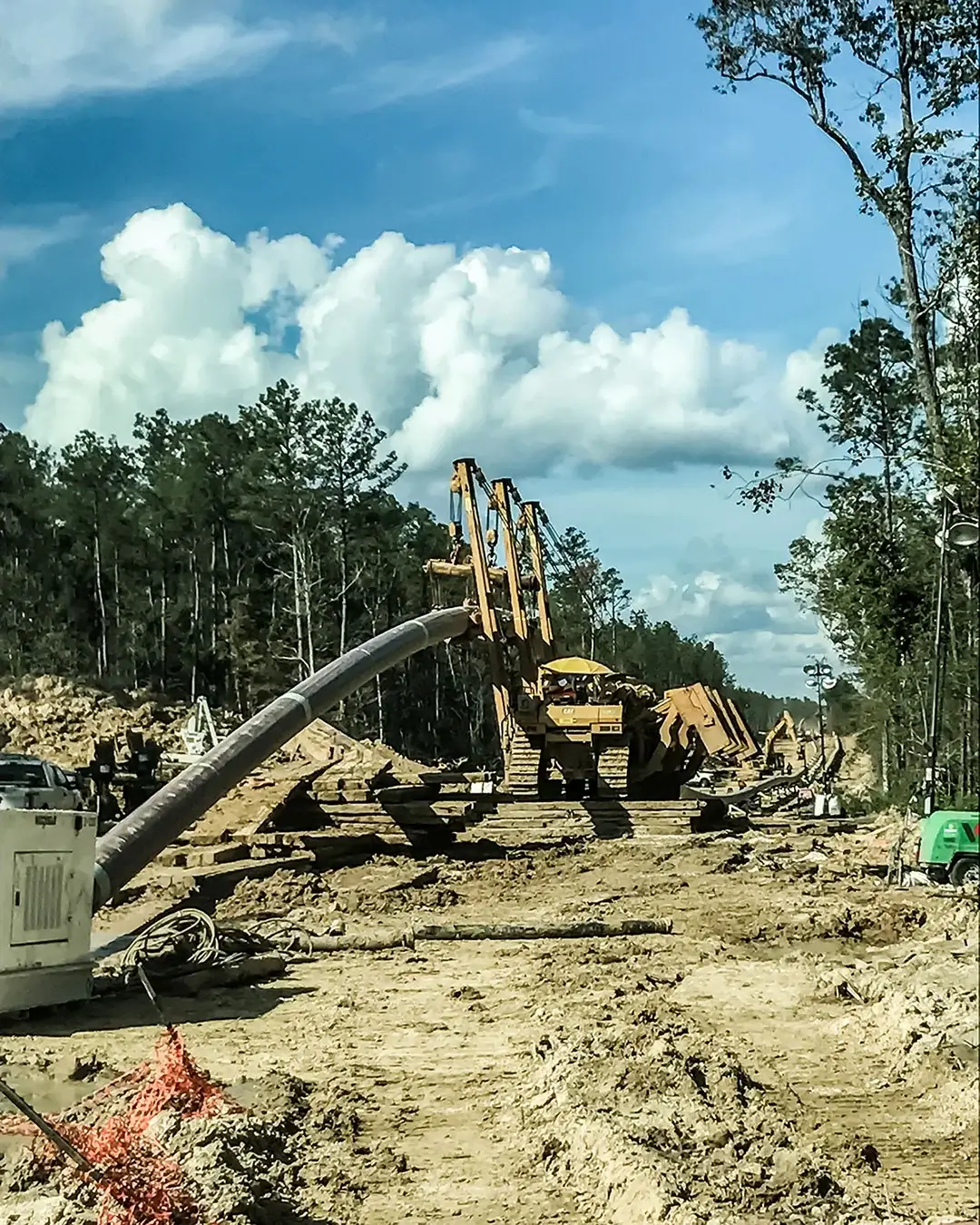 A large pipeline being transported by equipment through a forest.