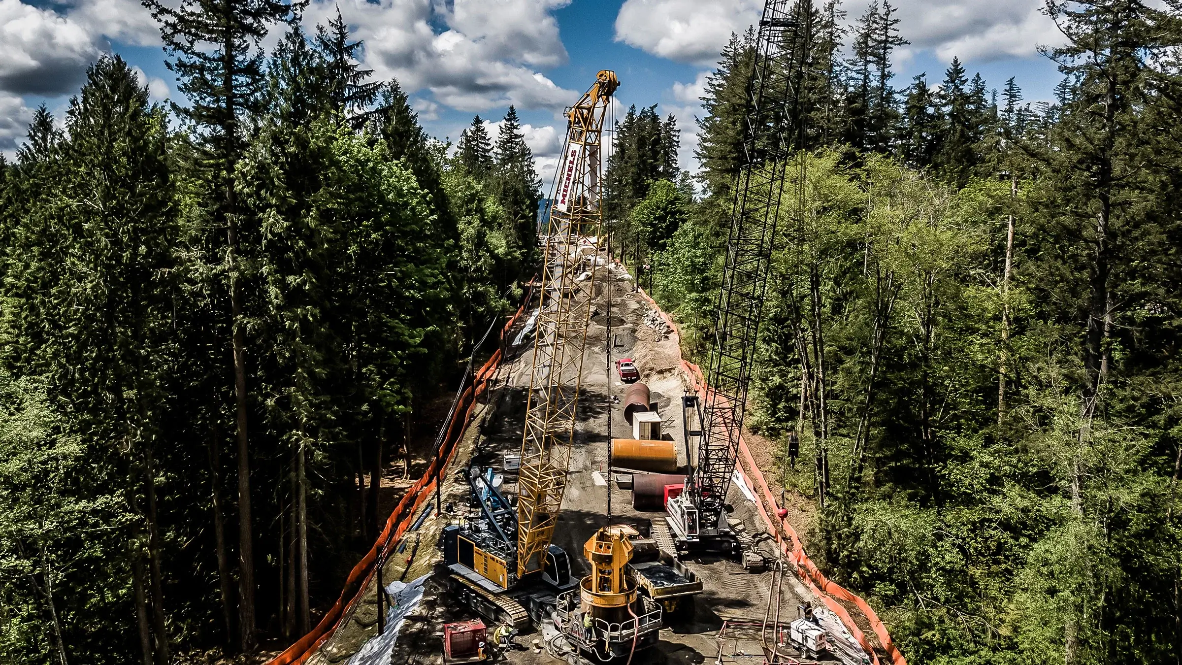 Multiple cranes and other large equipment work on a foundations project in a forest