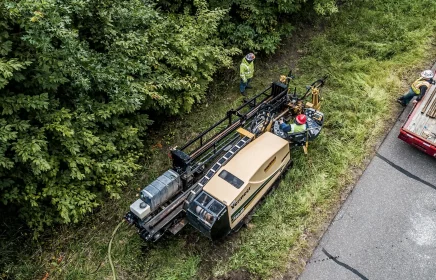 A small directional drill installs utility pipe near a roadside forest