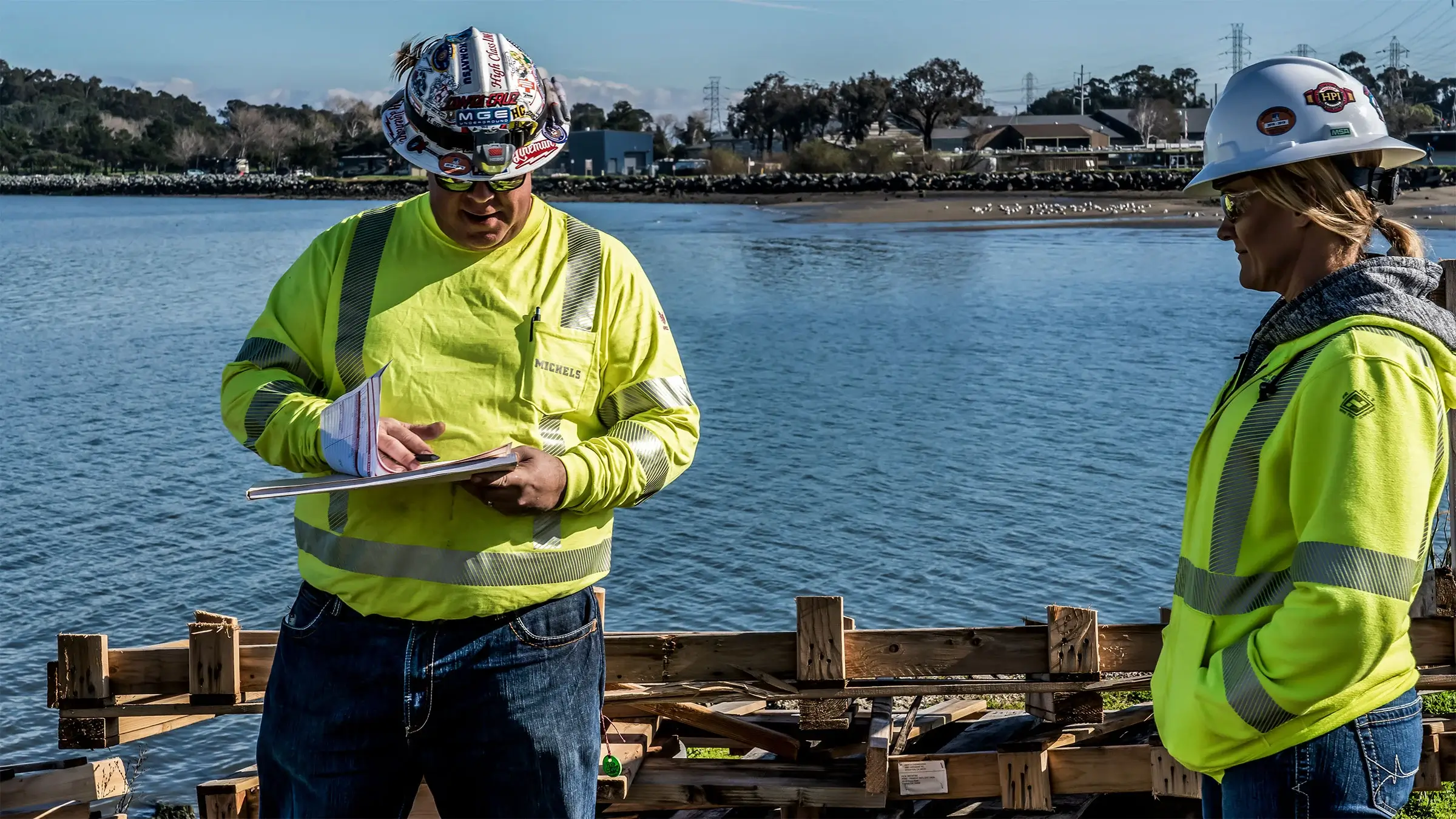 A project manager and an HSE manager review a job safety analysis document next to the ocean