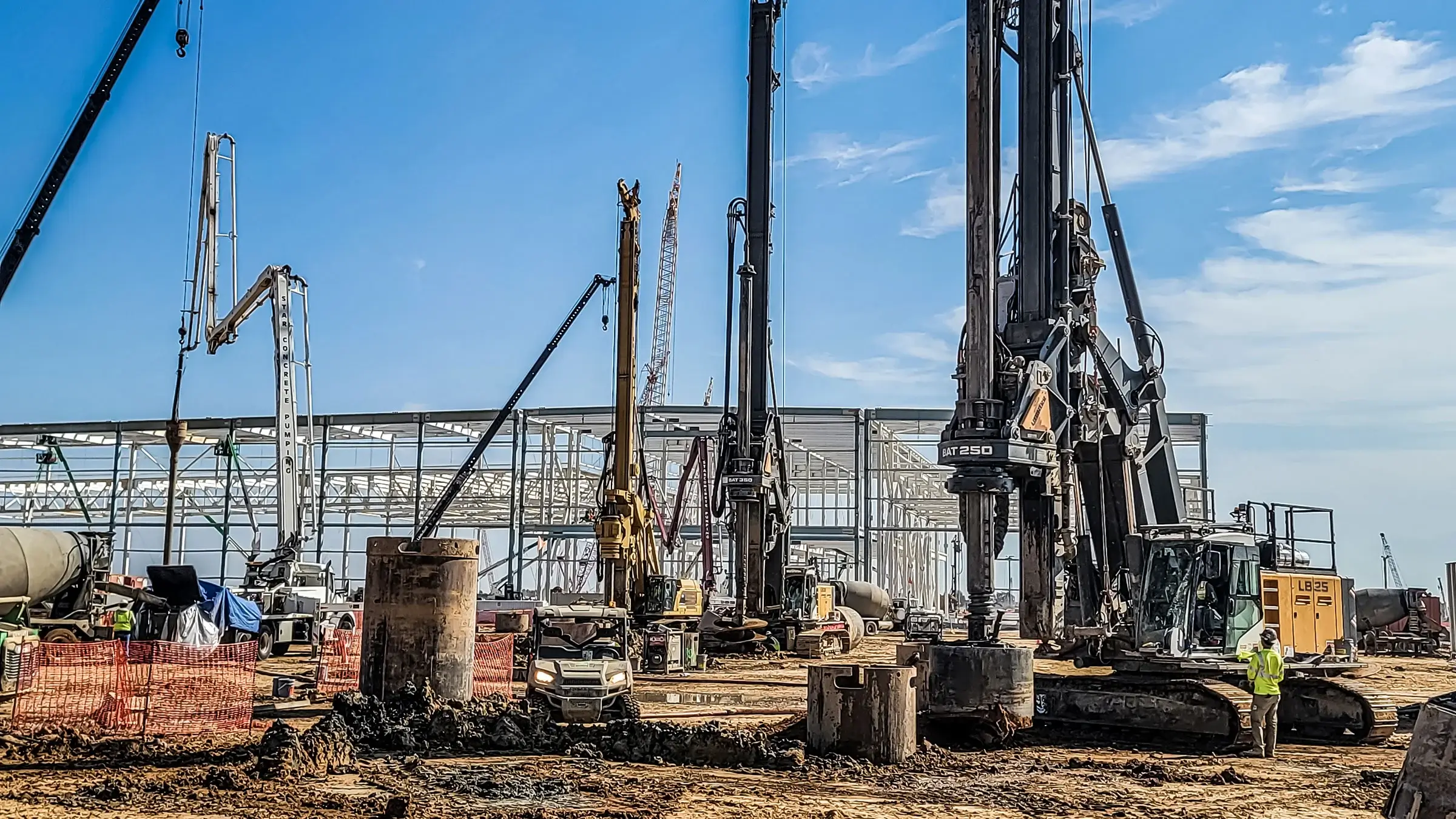 Work site on a sunny day, equipment includes a crane and other heavy equipment.