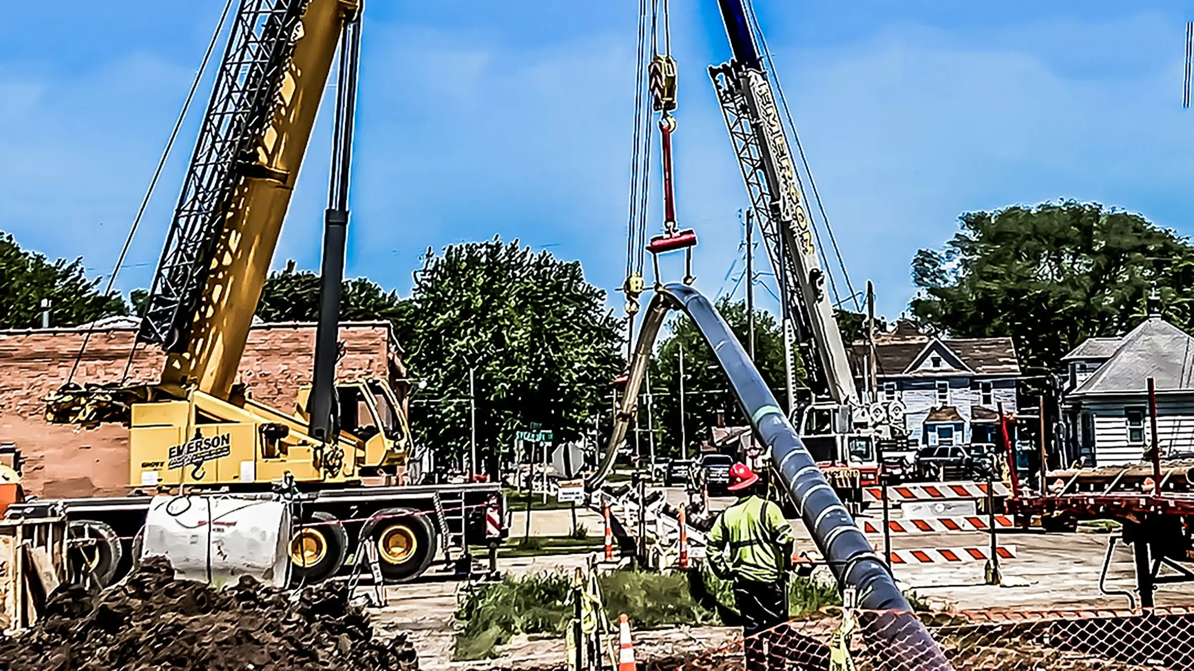 Several cranes assist in guiding pipeline into ground near residential homes