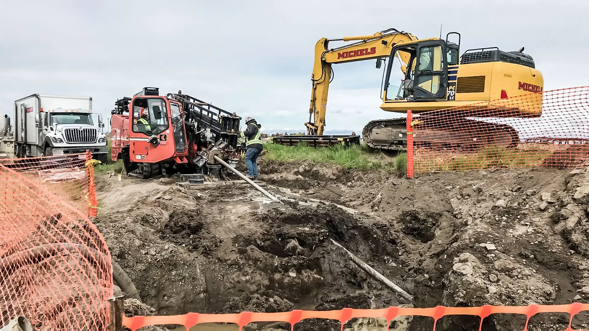 A small HDD rig and trackhoe operates on a dig site
