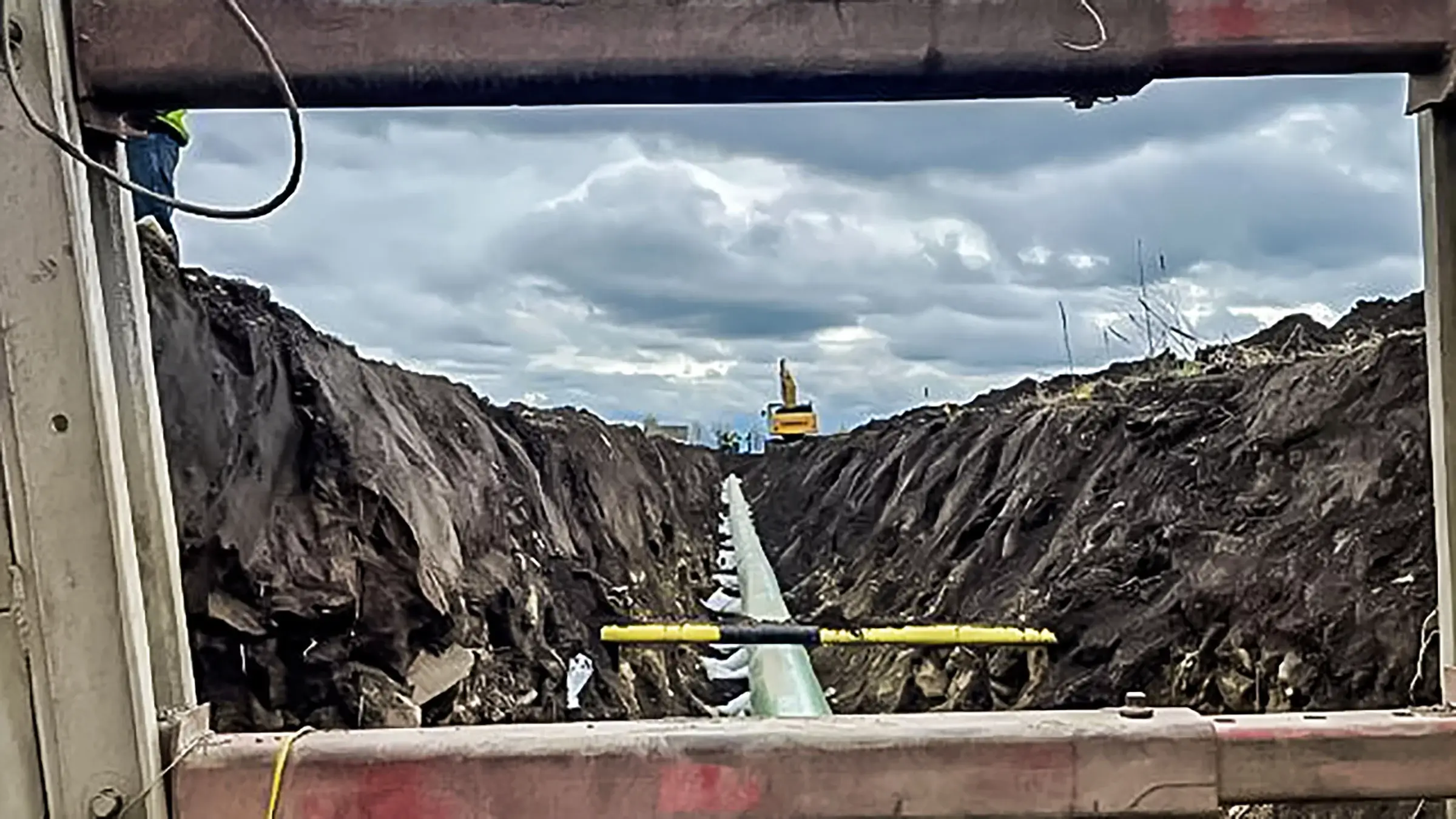 An excavator operates alongside a trench containing a pipeline