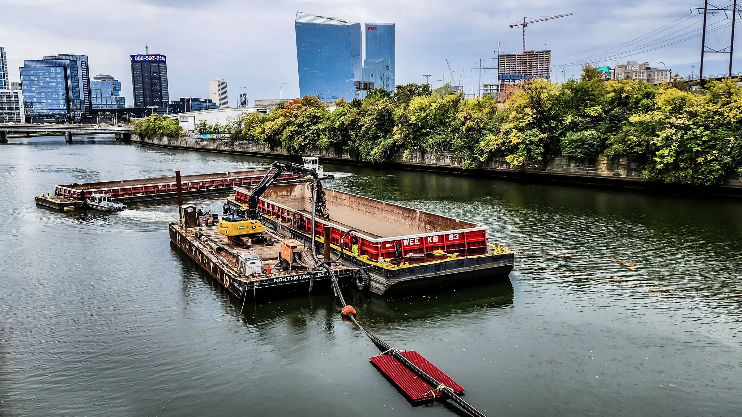 An excavator operates on a barge near several boats.