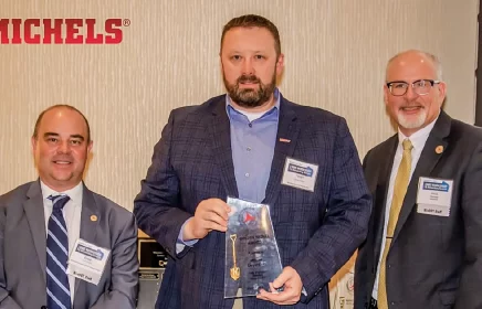 Man with award stands in between two other men