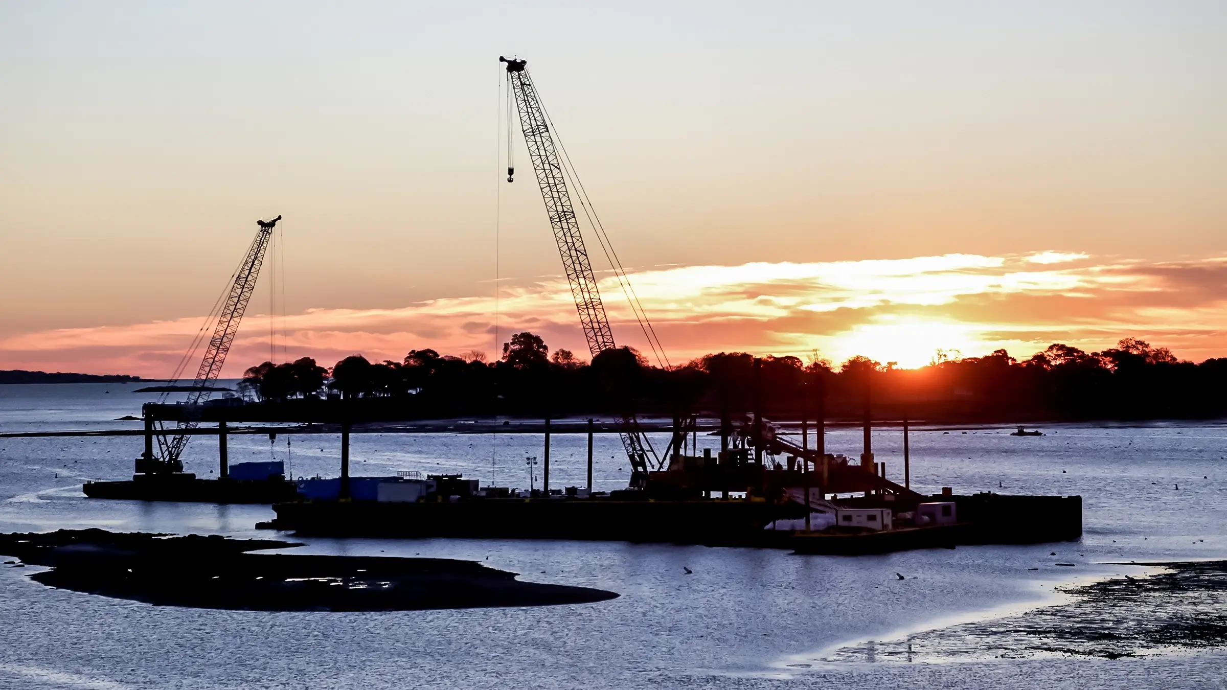 An HDD marine job site with two large cranes at sunset