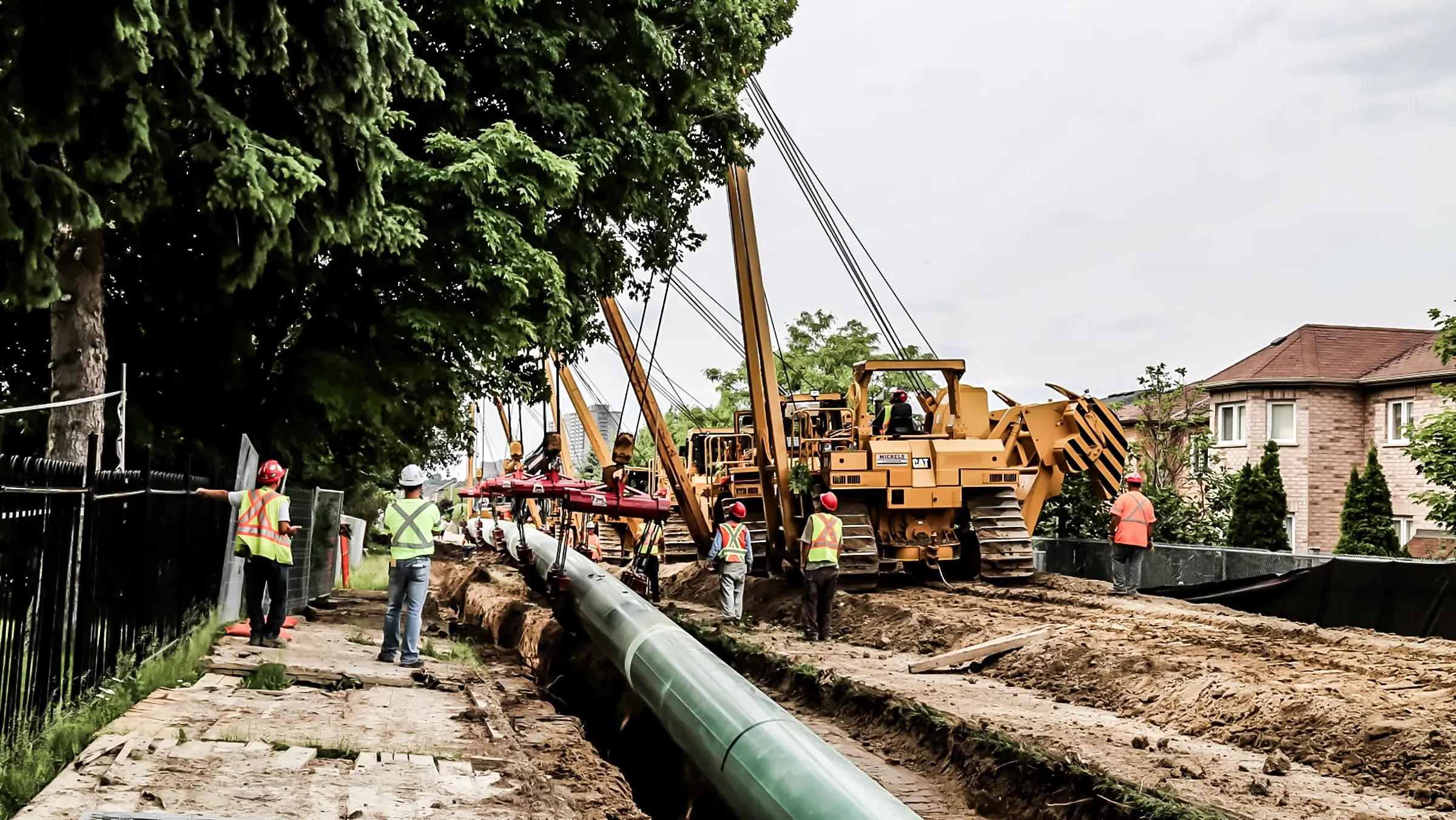 Several pipelayers lower a pipeline in a trench.