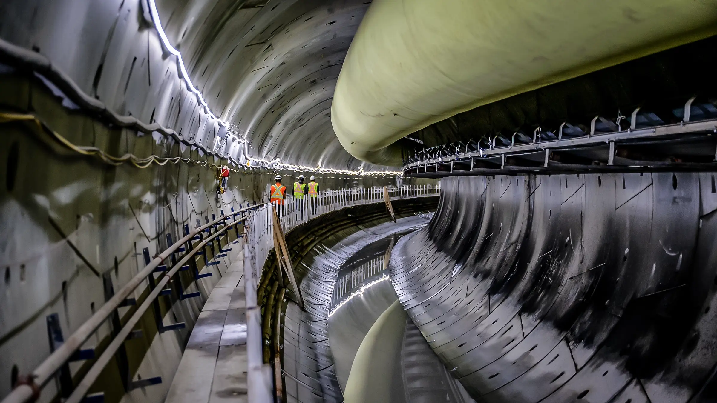 Several workers walk down a long underground tunnel.