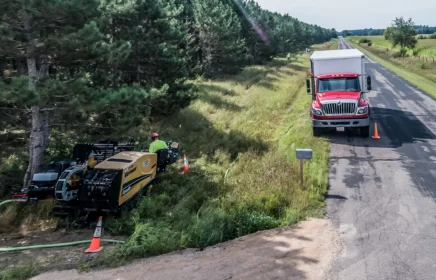 A small HDD rig and box truck work near a rural Wisconsin road.