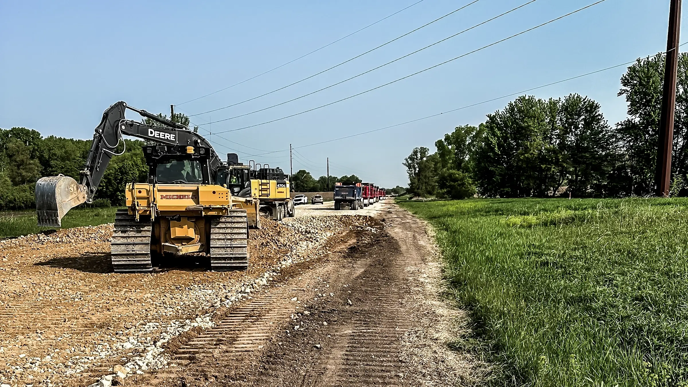 Several excavators and dump trucks operate along a road.