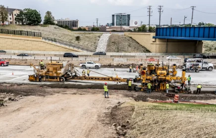 A paving crew operating near a bridge and busy highway.
