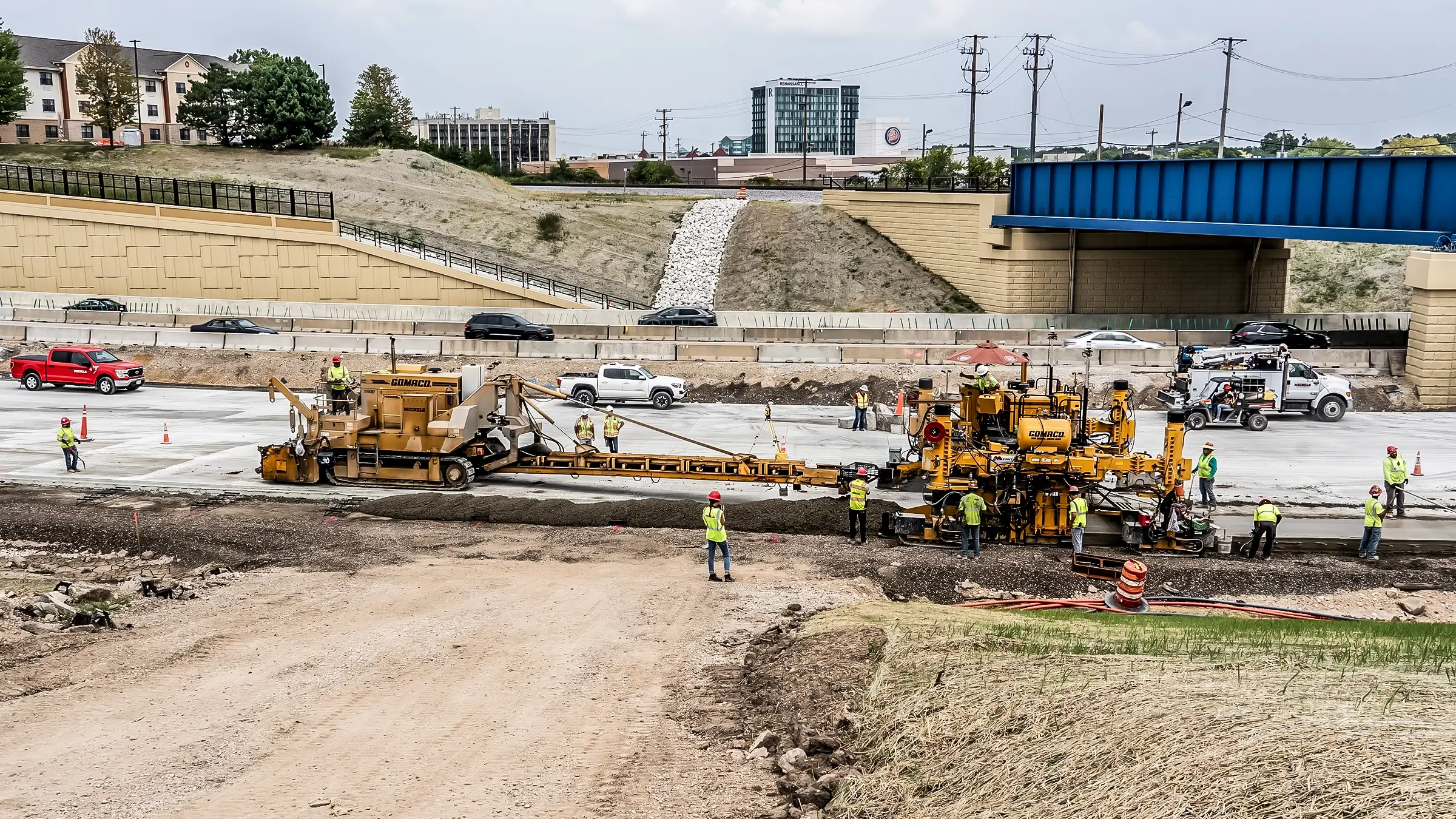 A paving crew operating near a bridge and busy highway.