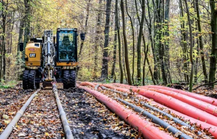 Equipment pulling cables through a rural wooded area.