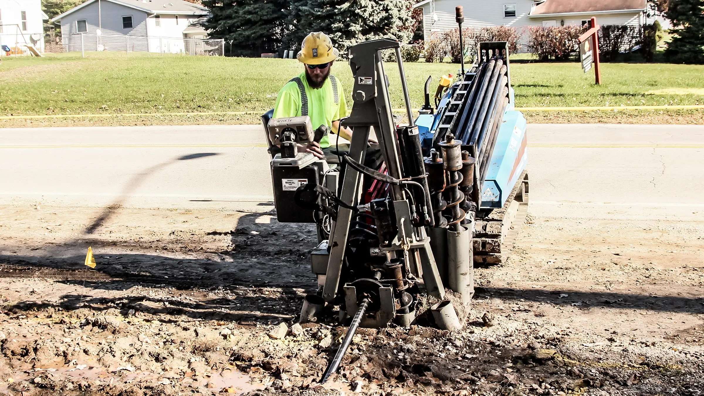 A crew member operates a small HDD rig near a roadside.