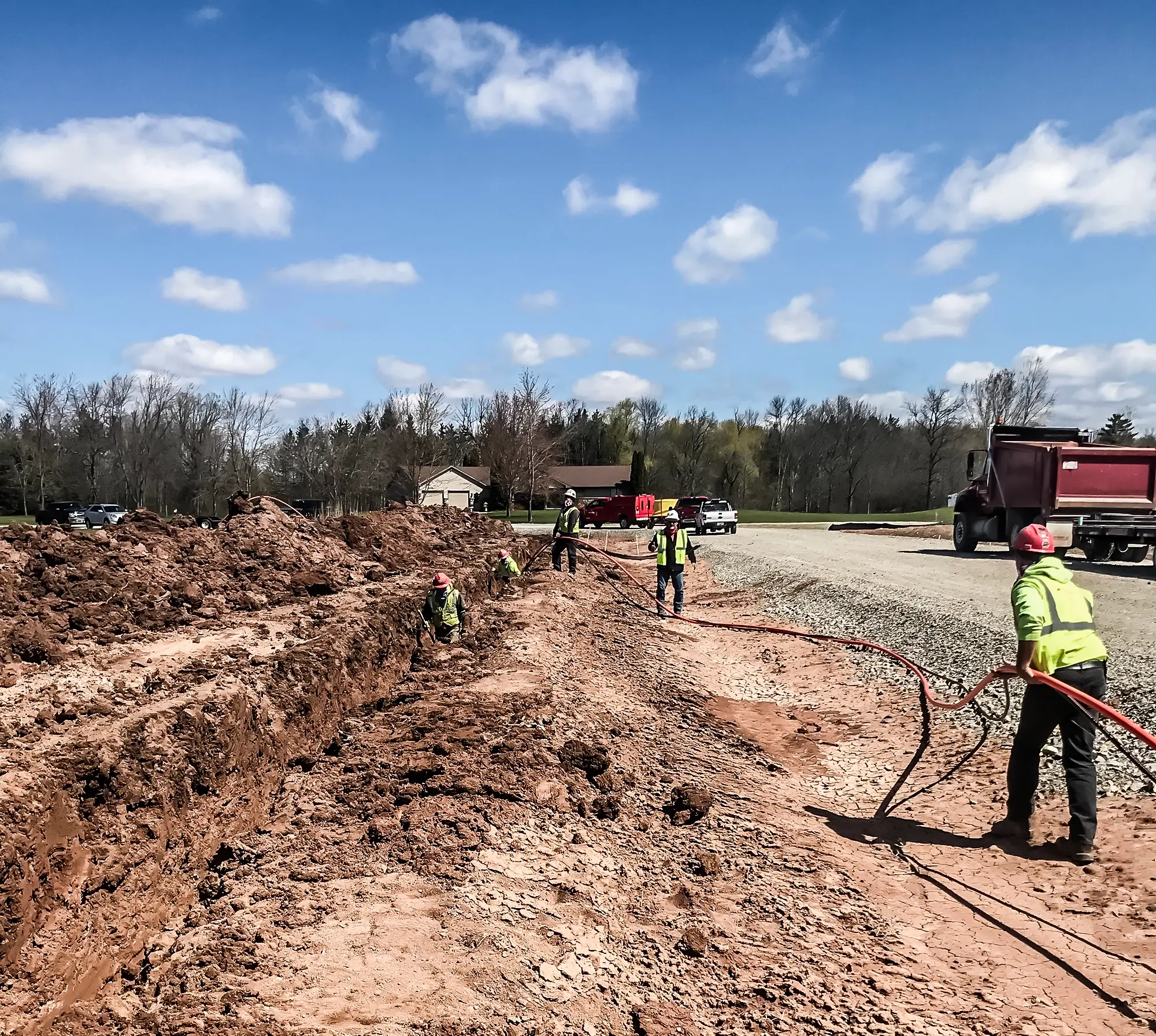 Several crew members operate on a joint trench installation near a roadside.