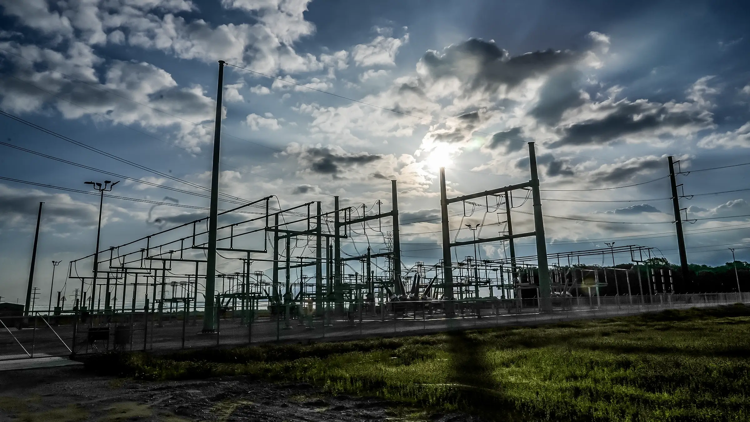 The sun shines through the clouds on a switchyard.