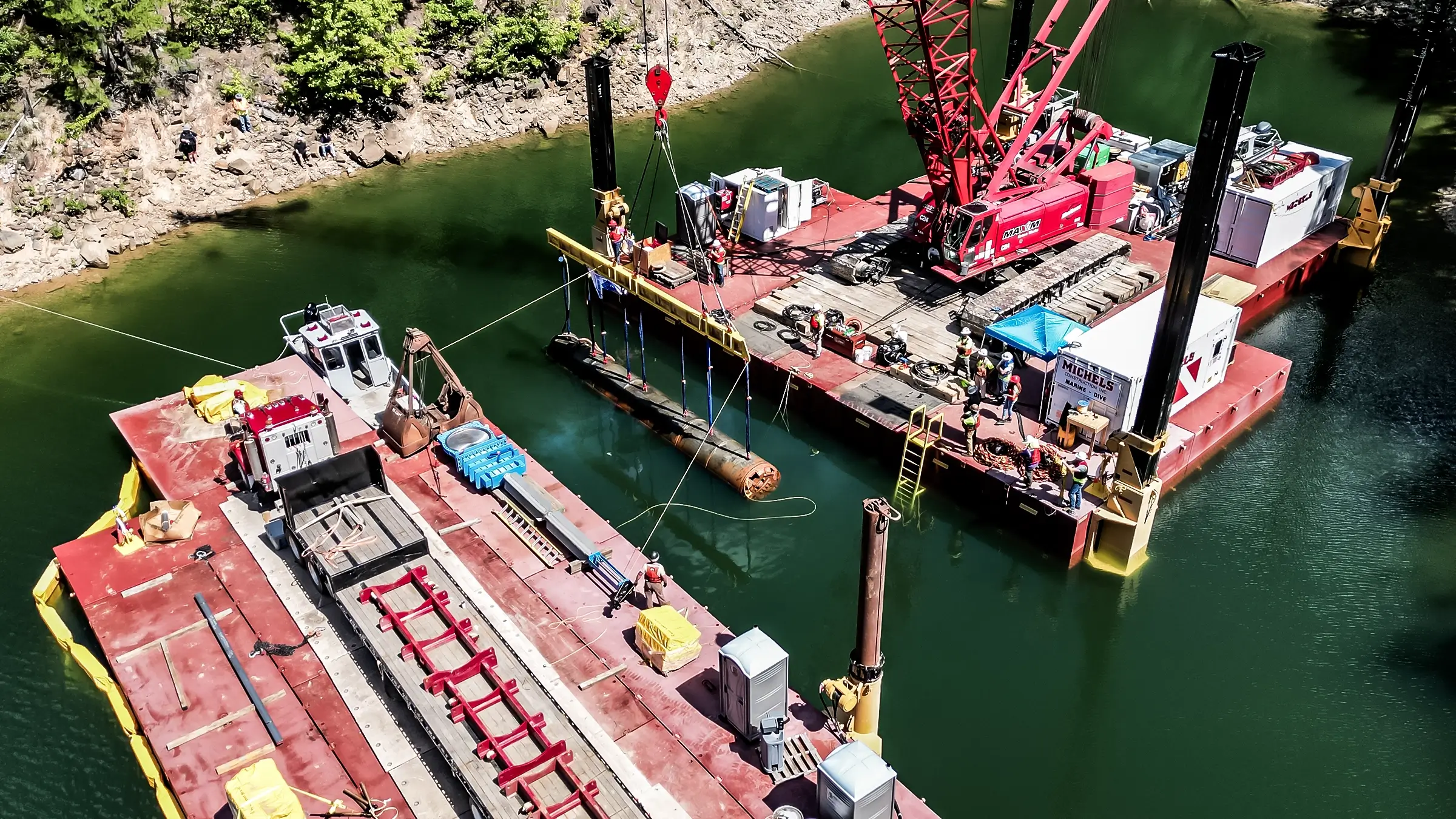 Two barges, one with a crane, lifts a portion of drilling equipment out of the water.