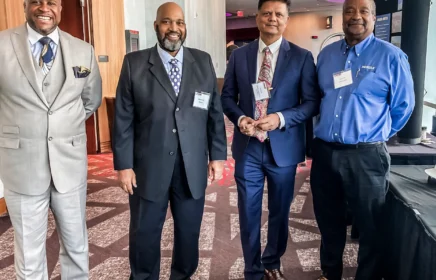 Four men in suits stand in a group at a Supplier Diversity event.