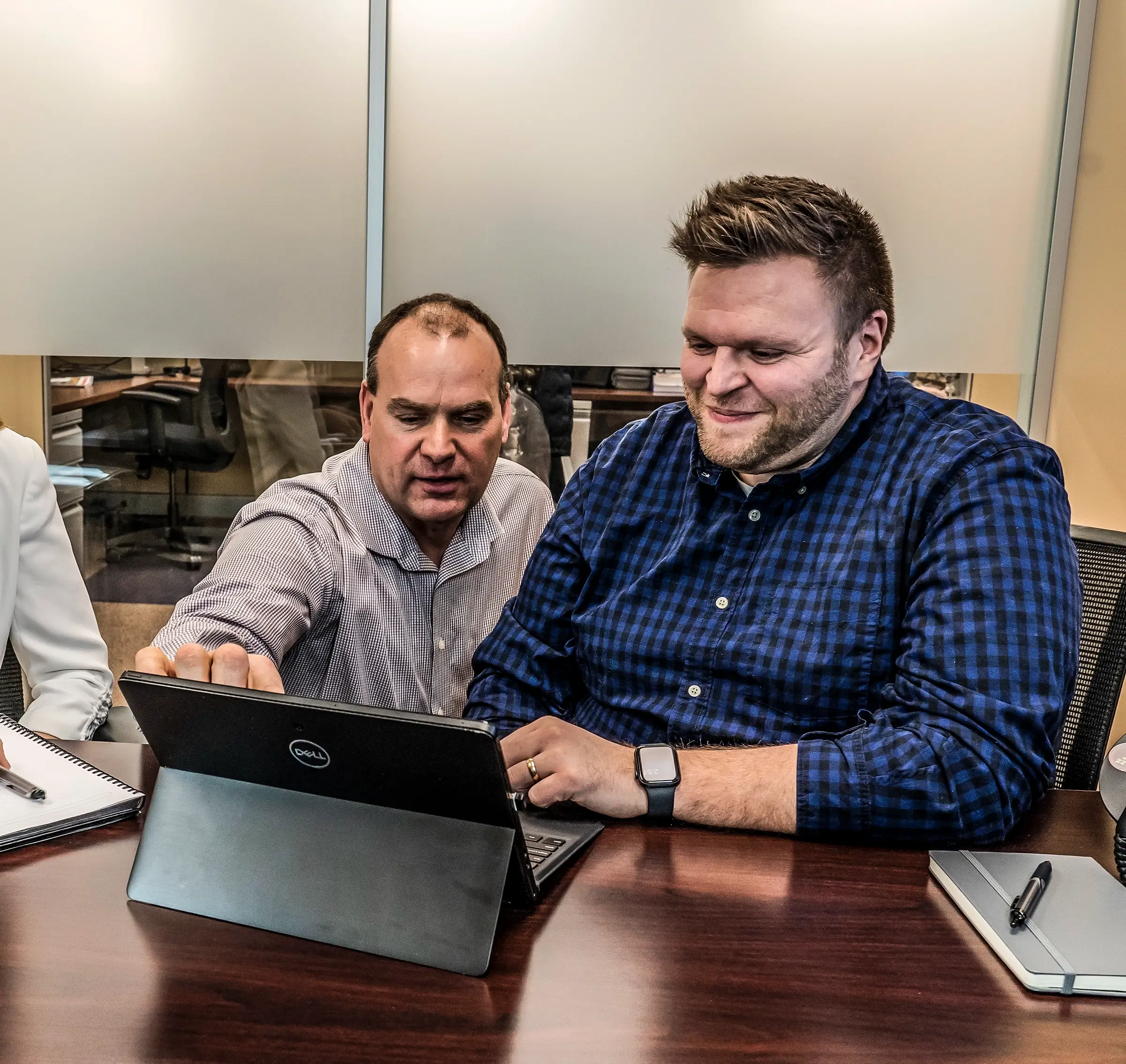 Two men look at a tablet in a conference room.